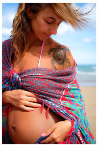 Smiling pregnant woman standing on beach against sky