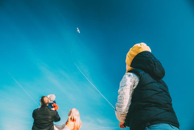 Low angle view of friends standing against blue sky