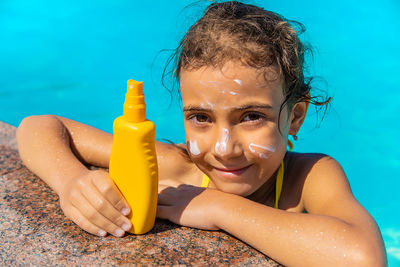 Portrait of smiling girl with suntan lotion in swimming pool