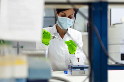 Female medical expert using pipette while testing in laboratory during pandemic