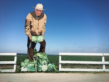 Portrait of man standing on bench against blue sky