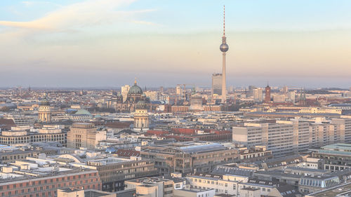 Fernsehturm amidst cityscape against sky during sunset