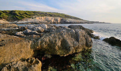 Scenic view of rocks on shore against sky