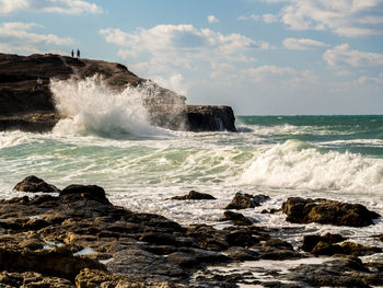 Waves splashing on rocks against sky