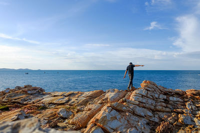 Man standing on rock by sea against sky