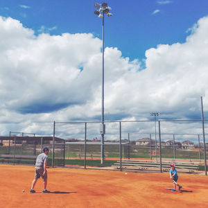 Father and son playing baseball on field against cloudy sky