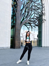 Full length of young woman standing against building