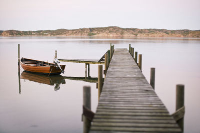 Motorboat moored by jetty over lake against clear sky