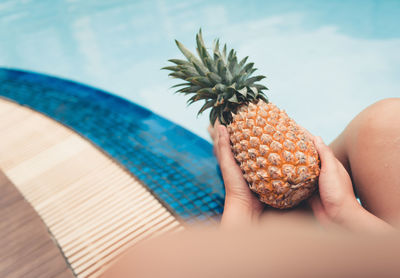 Midsection of person holding pineapple while sitting at poolside