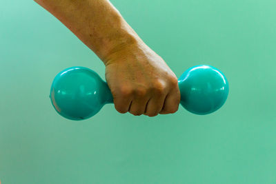 Cropped hand of man holding dumbbell against green background