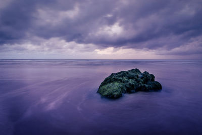 Rock formation at sea shore against cloudy sky during sunset