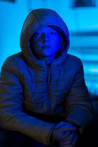 Portrait of young person sitting in room lit with only blue light