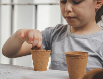 Caucasian girl planting seeds in a cardboard cup pushing her finger.