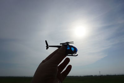 Cropped hand of person holding helicopter toy against sky during sunset