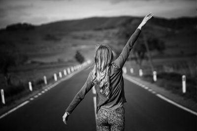 Rear view of woman with arms raised standing on country road