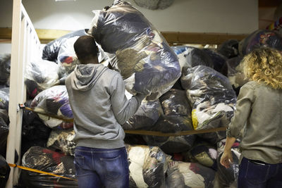 Rear view of coworkers stacking plastic sacks in warehouse