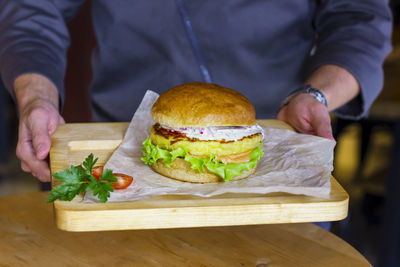 Vegetarian burger with potato cutlet, salad and sauce on wooden board in man hands