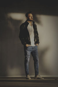 Young man looking away while standing against wall