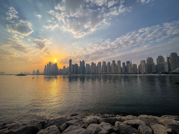 Sea by buildings against sky during sunset
