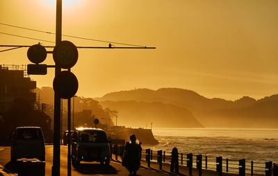 Silhouette people on street by sea against orange sky　during sunrise