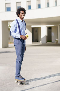 Portrait of young man standing on footpath against building