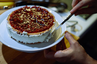 Person prepairing cake with whipped cream on table