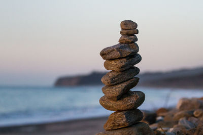 Close-up of stone stack at beach against sky during sunset