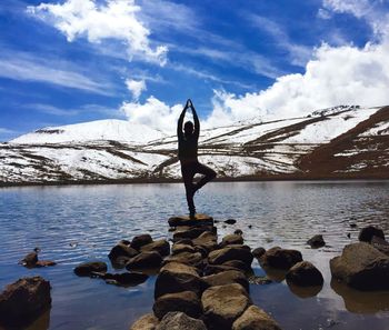 Man doing yoga on rock in lake against sky