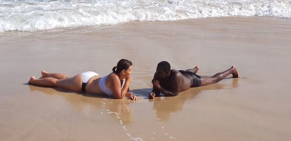 Full length of people wearing swimwear lying on shore at beach during sunny day