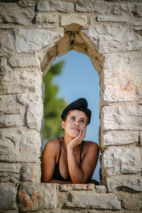 Thoughtful woman leaning on stone wall window