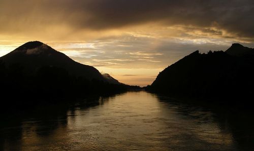 Scenic view of river and mountains against sky at sunset