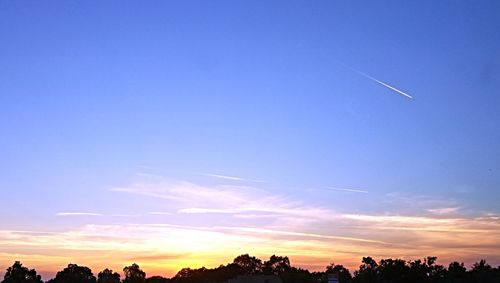 Low angle view of silhouette vapor trail against sky during sunset