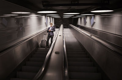 Low angle view of businessman with luggage checking time on escalator in airport