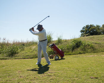 Full length of senior man playing golf on grass during summer