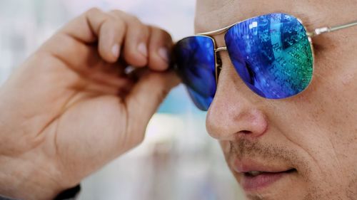 Portrait of handsome young man trying on blue sunglasses at optical store, optician retail store