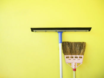 Close-up of cleaning equipment against yellow wall