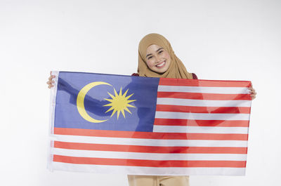 Portrait of cheerful young woman showing malaysian flag against white background