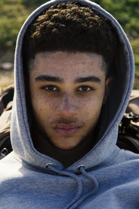 Young hispanic male with dark hair in gray hoodie looking at camera with serious gaze while lying on street of city