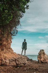 Rear view of man standing on rock by sea against sky
