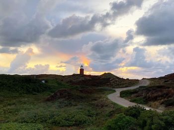 Lighthouse on field by buildings against sky during sunset