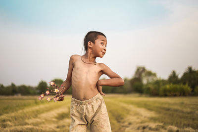 Boy holding flowers standing on grassy field against clear sky