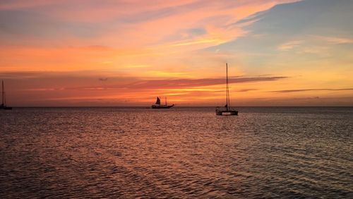 Silhouette sailboat in sea against romantic sky at sunset