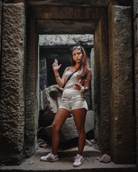 Full length portrait of young woman standing against wall