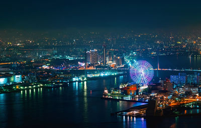 Illuminated ferris wheel by river in city against sky at night