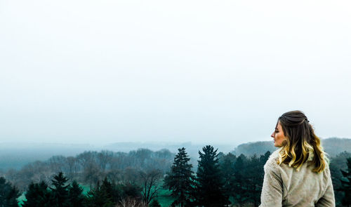 Rear view of woman standing in forest against sky during foggy weather