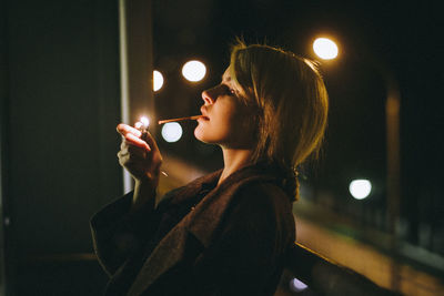 Woman smoking while standing against railing at night