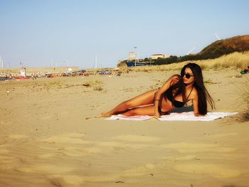 Woman lying down on sand at beach against sky