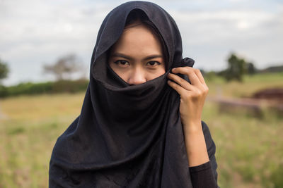 Portrait of smiling woman wearing headscarf covering face standing against sky
