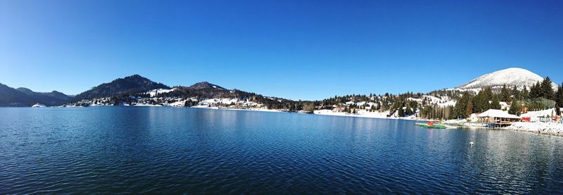 Panoramic shot of lake by mountains against clear blue sky