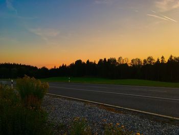 Road by trees against sky during sunset